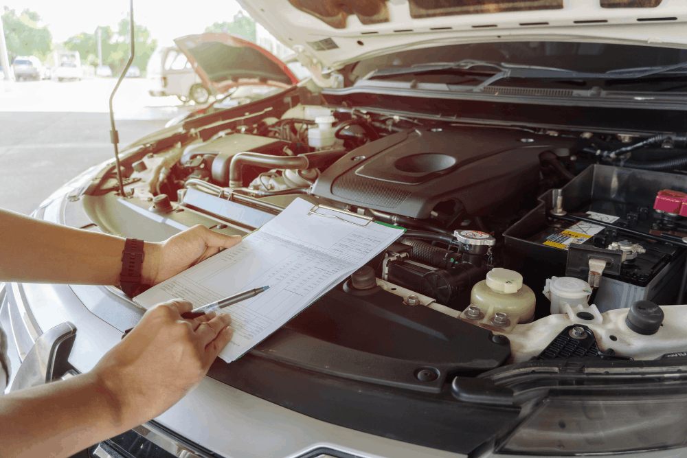Car safety check, auto repair in Smyrna, DE at Pristine Motorsports. Image of a technician reviewing a checklist beside an open engine bay to help identify maintenance needs and support vehicle reliability.